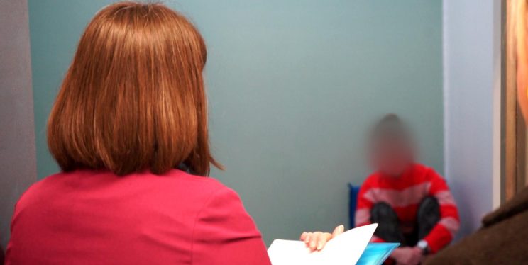 A woman in a police cell talking to a detainee with a clipboard