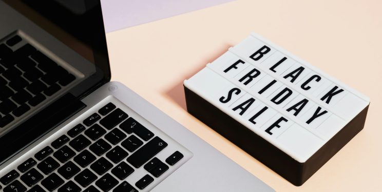 An open laptop is on top of a table. Next to the laptop is a sign that says Black Friday Sale.