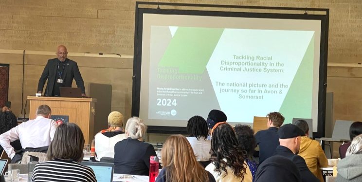 Desmond Brown presenting to an audience in City Hall - with the slide on Tackling Disproportionality featured