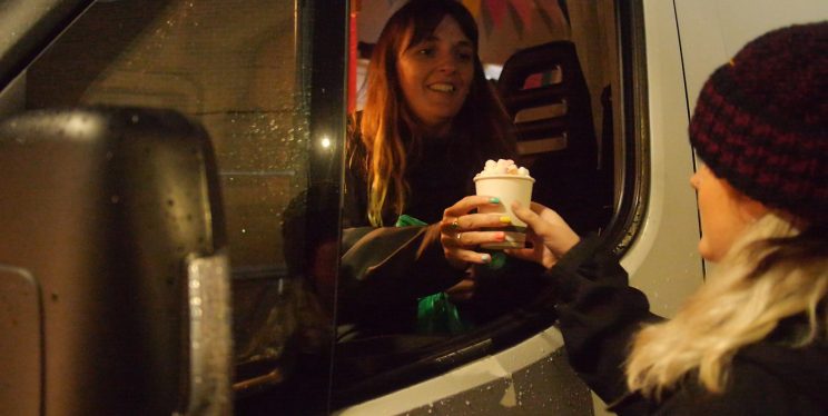 An image of a volunteer serving a woman a hot chocolate from their outreach van