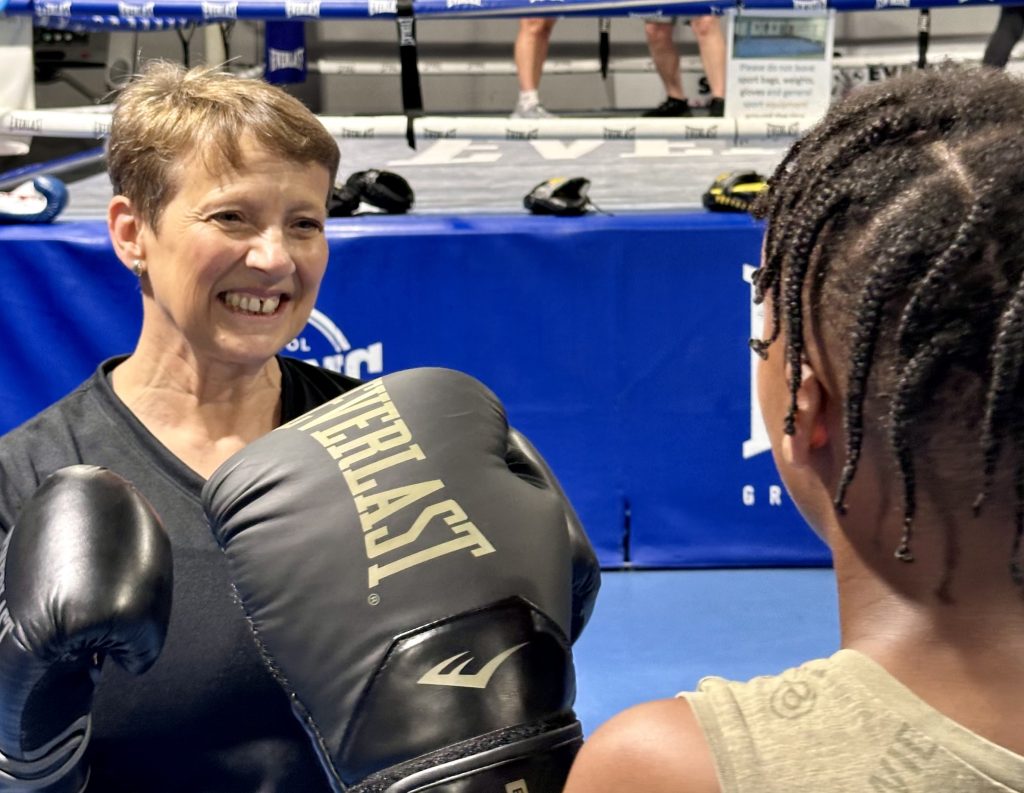 A smiling PCC Clare Moody and a young member of Empire Fighting Chance don boxing gloves and stand in front of the boxing ring together